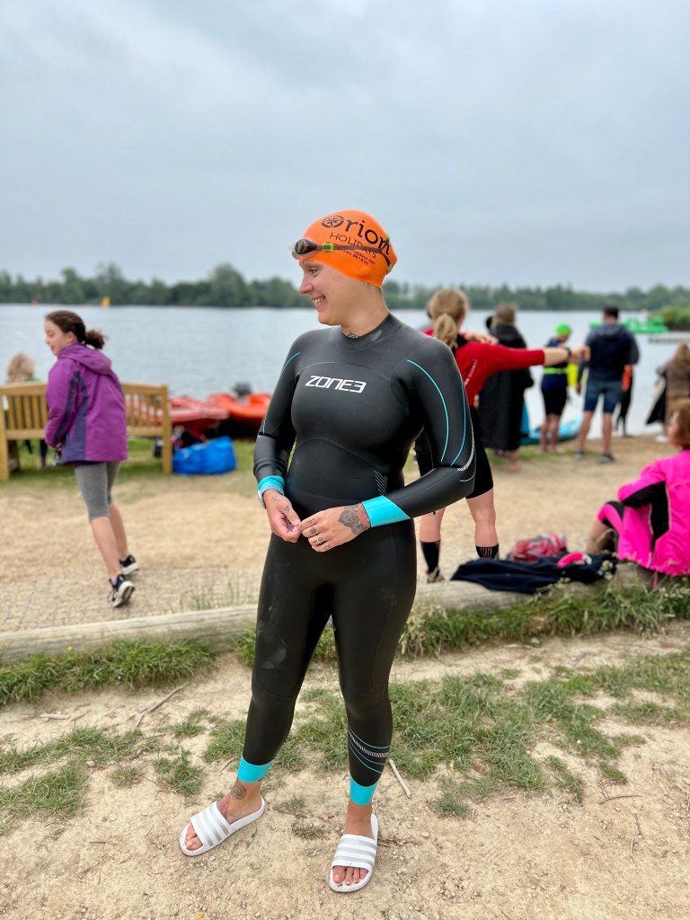A woman in a wetsuit stands by a lake ready to do an open water swim