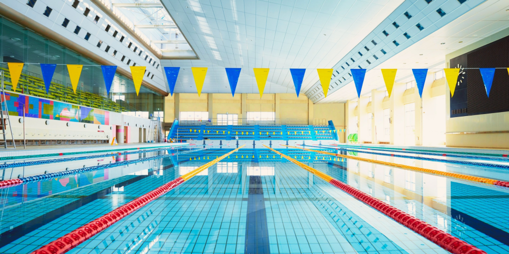 A large indoor swimming pool separated by lane dividers and there is bunting above the top of the pool