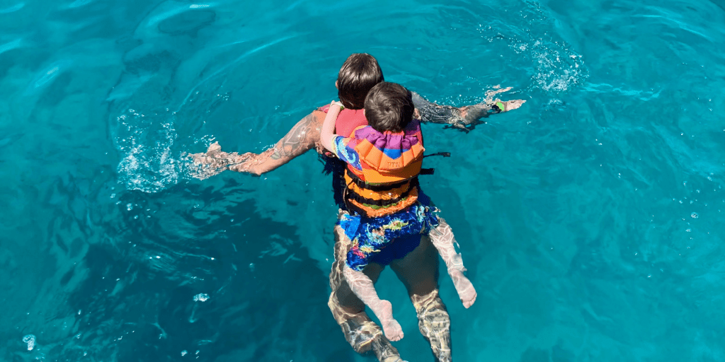 A little boy swims on his mum’s back in the sea